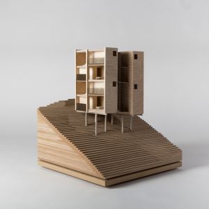 A model photo of a steep, terraced terrain with a cut building on stilts. Beds are placed in the cut rooms. MDF, grayboard.