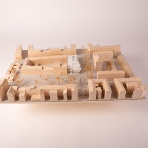 A model photo of an urban planning model of a dense urban area made of wood with an inserted design in acrylic. Grayboard, wood, acrylic.