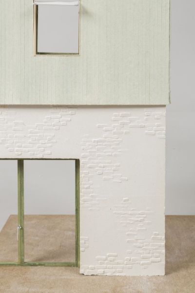A photo of a colored model with a whitebrick ground floor and a sage-colored wooden first floor. Green window frames.