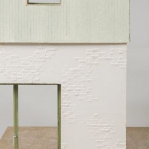 A photo of a colored model with a whitebrick ground floor and a sage-colored wooden first floor. Green window frames.