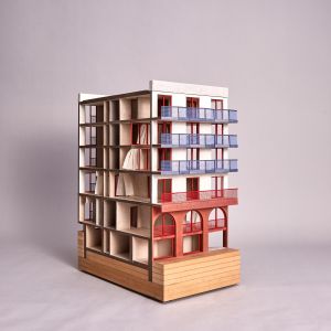Ein Schnittmodell eines mehrstöckigen Gebäudes mit blauen und roten Akzenten. MDF, Graukarton.
