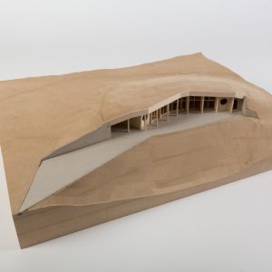 A model photo of a building sunken into a site. MDF, grayboard, wood. Lightweight construction.